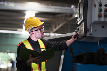 Male engineer control CNC machine in factory. Male technician working and repairing or maintenance CNC machine with safety uniform, helmet in industry factory