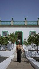 Sticker - Woman walking up steps toward a charming white hotel terrace in a sunny outdoor setting