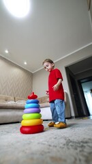 Poster - Four-year-old toddler constructs a toy pyramid on the floor. Kid changes the rings in correct order and size and runs away. Low angle view. Vertical video.