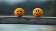 © Tcukimay - Two yellow smiley faces painted on round objects are sitting on a wooden beam.
