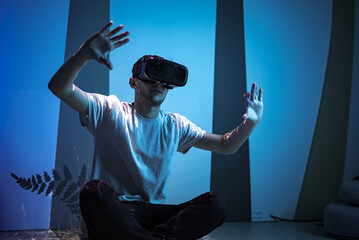 young man wearing vr glasses sitting in a yoga pose on the virtual reality escape room floor. fun, e