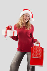 Wall Mural - Happy merry Christmas woman wearing Santa hat holds gift box and red shopping bags. Image for sale offer promotions, online shopping, advertising banner, poster, or gift card, isolated background