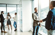 © peopleimages.com - Professional, men and meeting with handshake by window for negotiation, partnership and project agreement. Corporate, people and deal with introduction for recruitment, thank you and b2b promotion