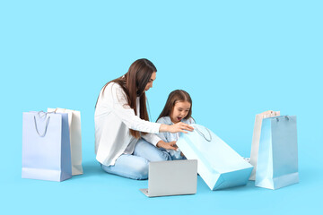 Wall Mural - Happy mother with her little daughter shopping online on blue background