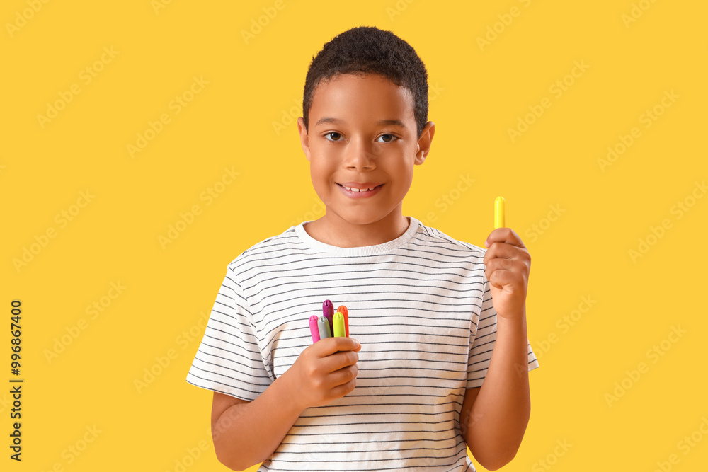 Little African-American boy with felt-tip pens on yellow background