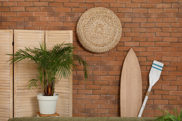 Sticker - Surfing board, paddle and houseplant near brown brick wall in living room