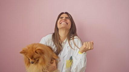 A joyful young woman in a lab coat holds a pomeranian dog against a pink background, epitomizing happiness and companionship.