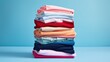 © Iona - An artfully stacked pile of neatly folded clothes in various colors against a blue background symbolizes organization and tidiness.