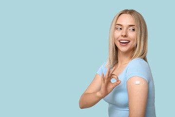 Canvas Print - Young woman with medical patch on arm showing OK against blue background. Vaccination concept