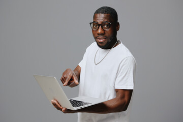 Smiling man holding a laptop in a casual white t shirt with glasses, demonstrating engagement in a modern work setting Background features a neutral grey color