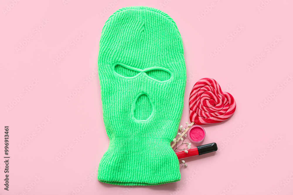 Composition with balaclava, lollipop and cosmetics on pink background