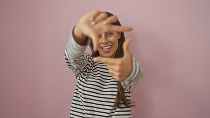 Poster - Smiling young hispanic woman making framing gesture with hands against a pink isolated background, portraying creativity and positivity.