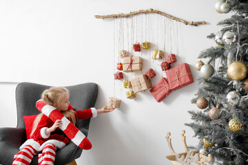 Poster - Cute little girl sitting in armchair and Christmas advent calendar hanging on light wall in room