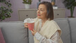 © Krakenimages.com - Mature woman sitting comfortably indoors holding a mug, in a house with a neutral color scheme and tasteful decor.