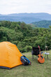 © VR Studio - A small orange tent is set up in a grassy field with a guitar and a backpack nearby. Concept of adventure and relaxation, as the person who set up the tent is likely preparing for a camping trip