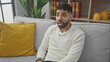 © Krakenimages.com - A surprised hispanic man with a beard sitting on a gray sofa in a cozy living room