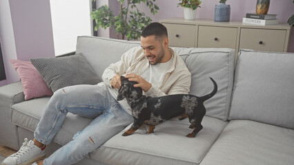 Canvas Print - Hispanic man enjoying time with his dachshund dog in the cozy living room of an apartment.