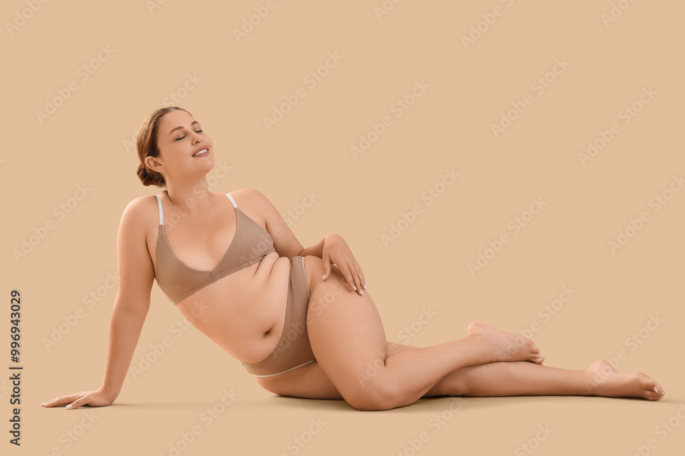 Beautiful plus size woman in underwear lying on beige background