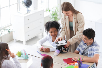 Wall Mural - Female teacher showing VR glasses to little pupils at table in classroom