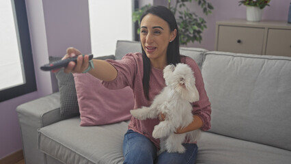 Hispanic woman holding a white dog watching tv in a cozy living room