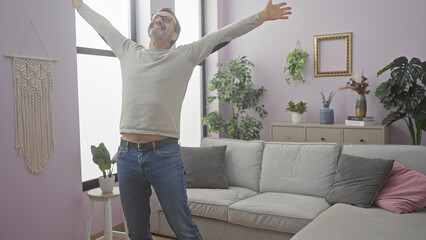 Wall Mural - Middle-aged man celebrating happily in a cozy living room, expressing joy and freedom.