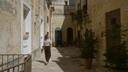 Wall Mural - A young hispanic woman walks down a charming alley in lecce, puglia, italy, enjoying the historic architecture and vibrant atmosphere.