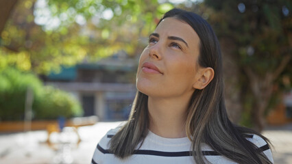 Wall Mural - A contemplative young woman enjoys a tranquil moment in a sunny urban park setting, exuding natural beauty and calmness.