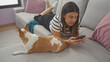 © Krakenimages.com - A woman lies on a sofa using a smartphone with a chihuahua dog beside her in a cozy living room.