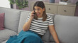 © Krakenimages.com - Smiling woman speaking on smartphone while relaxing comfortably on a couch inside her modern apartment.