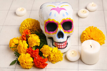 Wall Mural - Painted human skull, marigold flowers and burning candles on light tile background. El Dia de Muertos