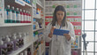 © Krakenimages.com - A young hispanic female pharmacist in a white coat reviews inventory on a tablet inside a well-stocked pharmacy.