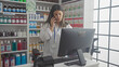 © Krakenimages.com - A focused woman pharmacist talks on a phone in a well-stocked drugstore with a variety of products on the shelves.