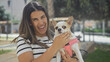 © Krakenimages.com - A young, beautiful hispanic woman is smiling while holding her chihuahua dog in a lively urban park setting.