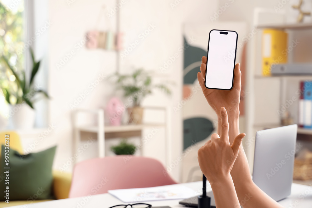 Woman pointing at blank mobile phone in office, closeup