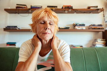 Stressed senior woman sitting on couch holding her head