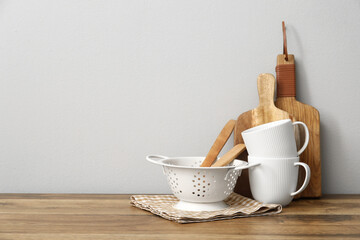 Wall Mural - Colander, wooden utensils and cups on table near white wall