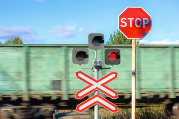 Stop sign before a railroad crossing. A passing train before a closed railroad crossing. Road signs.