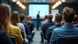 © cabado - Modern conference room filled with attentive diverse audience listening focused on blurred professional speaker presenter man or college teacher presenting with projection screen in distance at front.