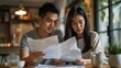 © Pat J. - Asian couple looking anxious and sad, holding bills and discussing financial issues at home