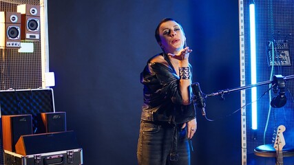 Bold grunge rock star sending air kisses from the stage to her fans, showing confidence and acting flirty with her audience at the club. Female artist performer being playful during concert. Camera A.