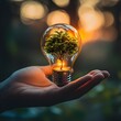 © Alpha - A close-up of a person's hand grasping a glowing bulb with a miniature tree sprouting inside, symbolizing growth, innovation, and nature