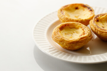 Stack of Portuguese sweet dessert egg tart or Pastel de Nata on white ceramic plate on white table. Copy space. Selective focus.