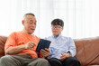 © JU.STOCKER - Asian Senior man and grandson using tablet smartphone doing a video call in living room
