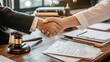 © Pannin - Confident lawyer shaking hands with her client over a wooden desk filled with legal papers, a gavel, and reference books, representing trust and professionalism in legal services.