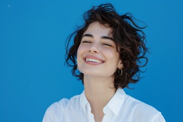 Smiling brightly, a Caucasian woman in a white shirt poses confidently against a turquoise backdrop, highlighting her charm and beauty.