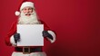 © Nadin Faust - santa claus holding an empty white sign board for christmas or new year banners, isolated on a red background with copy space for text, featuring a smiling santa in costume for festive advertising