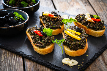 Tasty bruschetta with tapenade served on black stony board on wooden table
