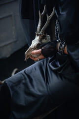 witch black dress woman holding old animal skull, dark abstract natural background. esoteric spiritual ritual for Samhain, Sabbath, Halloween. Magic, witchcraft, mystical practice.