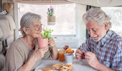 Wall Mural - Cheerful senior couple in travel vacation leisure inside a camper van dinette enjoying breakfast together.