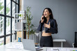 © apichat - A woman is talking on her cell phone while standing in front of a desk